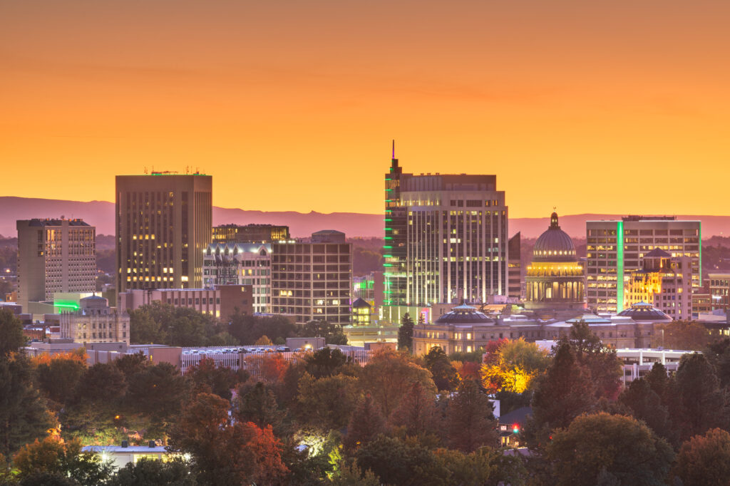 Cozakos and Centeno : City skyline at sunset with illuminated buildings and a clear orange sky.