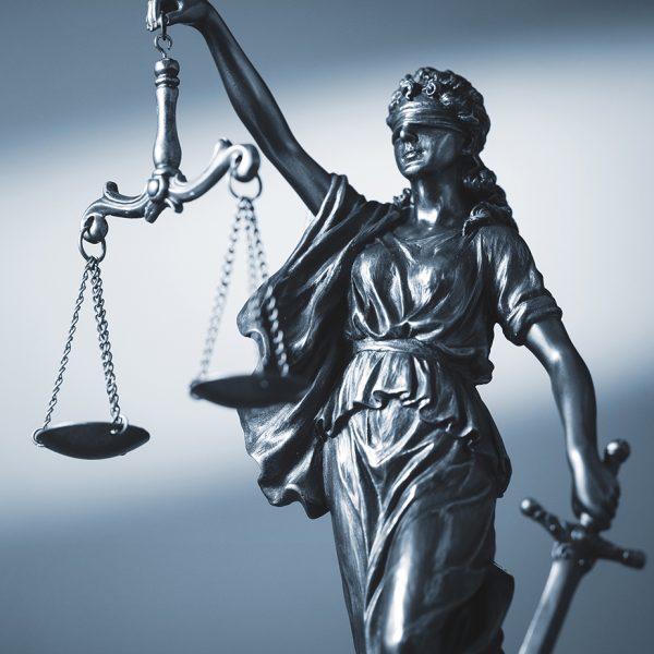 Blindfolded figure of Justice holding scales and a sword conceptual of the courts, judgement, law and order in a beam of light over a grey background with copy space